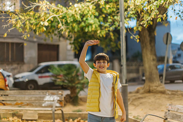 10 years old Boy in a yellow vest waves to someone in the park during evening, with soft lighting and a peaceful atmosphere. Horizontal image with copy space.