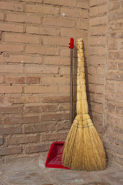 Close-up of a natural sorghum broom and red plastic dustpan in the corner by the brick wall. Concept background of hygiene and home cleaning.