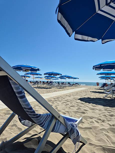 istock Empty Deckchair on Sandy Beach Under Blue Umbrellas - Summer Vacation Concept 2223411608