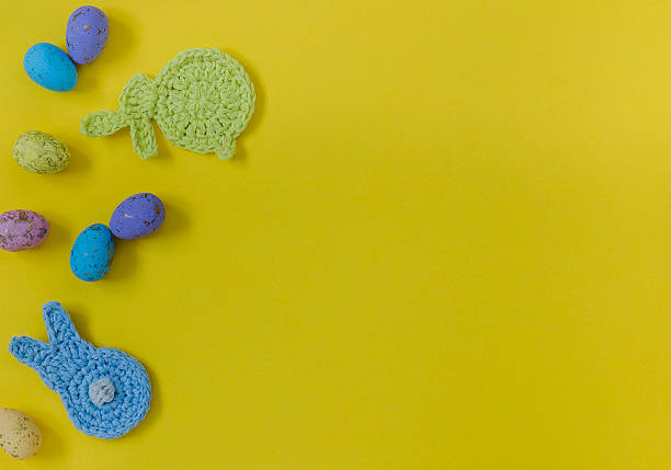 Easter composition with crochet bunnies and colorful eggs on a yellow background. Top view. Copy space.