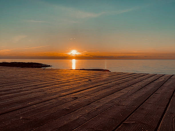 istock Low Angle of Boardwalk as Sun Rises Over a Calm Lake 2223425112