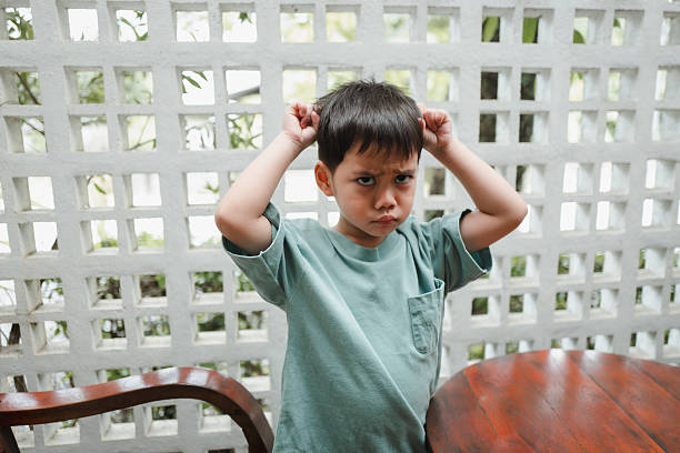 Young boy with an angry expression, scratching his head in confusion and frustration, reflecting the challenges of childhood learning