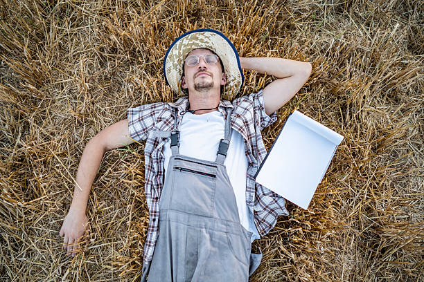 A farmer reclines peacefully in a straw-covered field, taking a break amid a summer day.