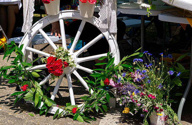 White painted wagon wheel decorated with fresh flowers and green branches, surrounded by colorful wildflower bouquets during an outdoor folk or rustic-style event.