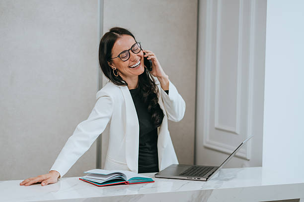 istock A joyful woman in a white blazer laughs while talking on the phone, embodying joy and connection in a modern setting. 2223440616