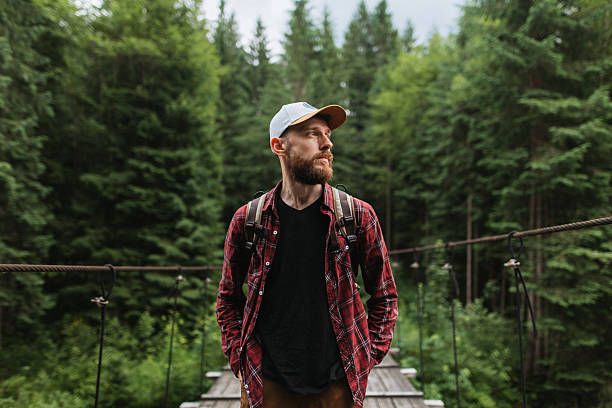 A man with a backpack walks across a wooden bridge surrounded by lush forest, embracing nature's beauty and tranquility while exploring the great outdoors on an adventurous journey