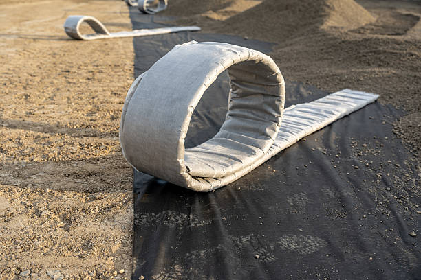Construction photo of a roll of flat panel drainage pipe being installed on a synthetic turf multi use athletic field.