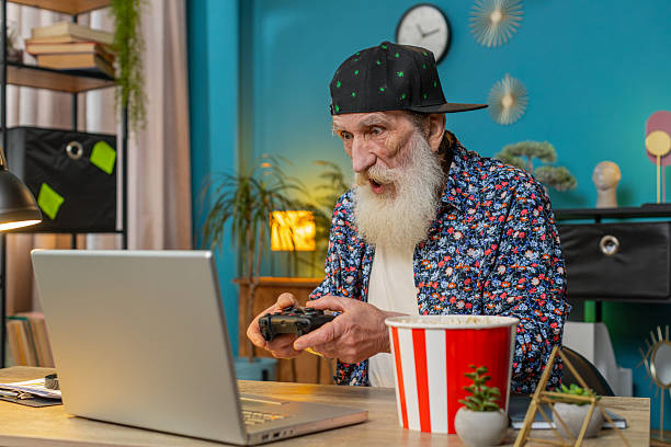 istock Excited happy senior man celebrating victory in play video game on laptop using controller joystick 2223454235