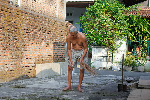 Asian man is cleaning the yard sweeping with a broom