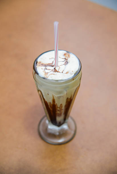 Thick chocolate milkshake with a retro paper straw in a glass tumbler with a teal background and copy space