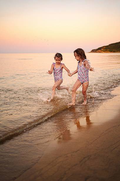 Two little sisters holding hands and running on the beach at sunset
