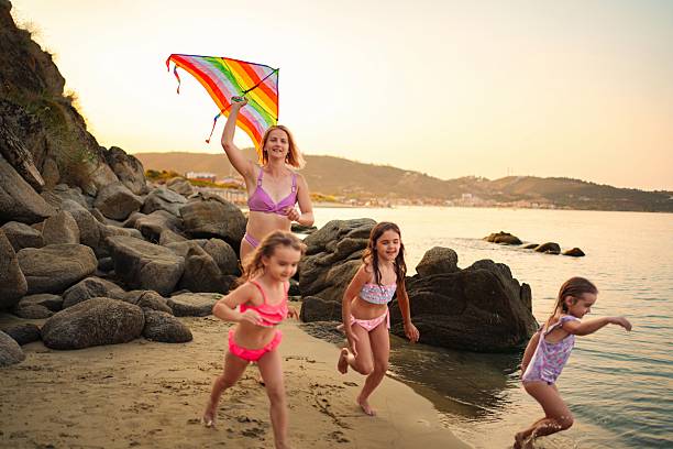 wide angle view of father and child flying a rainbow kite on sandy beach on a sunny day standing next to the sea