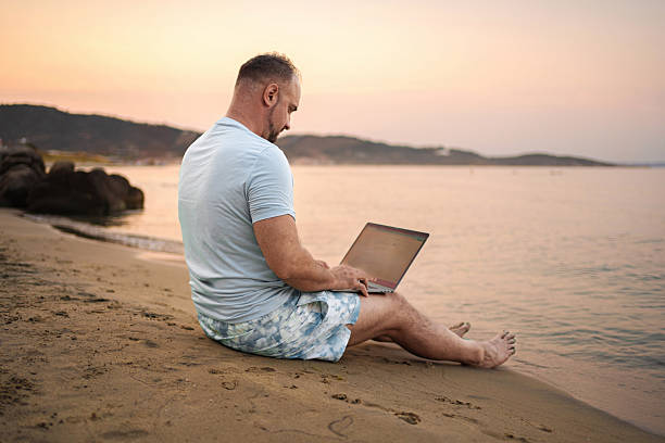 istock Man working on laptop at the beach during sunset 2223461557