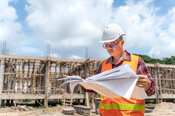 istock Asian engineer in a hard hat examining blueprints at a construction site. 2223475439