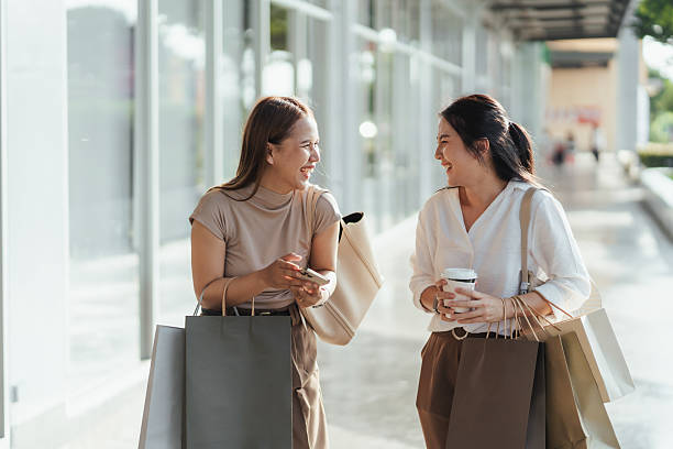 istock Two Asian women smiling and talking while walking outdoors after a successful shopping spree. Holding paper bags and coffee, they enjoy lively conversation, capturing friendship and modern lifestyle. 2223477888