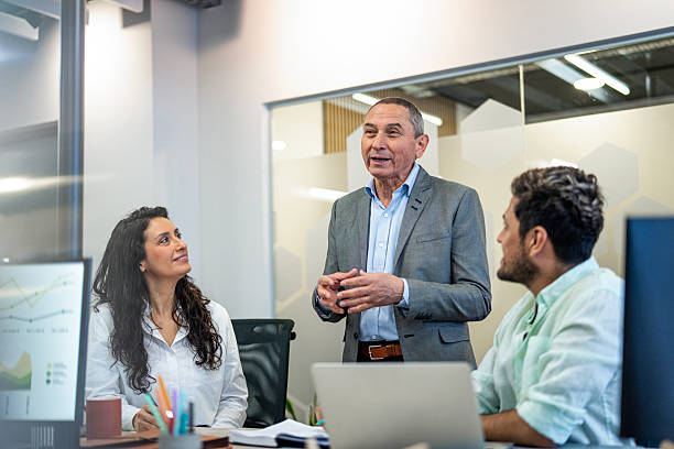 istock Senior executive reviewing project plans with younger employees inside office workspace. 2223478675