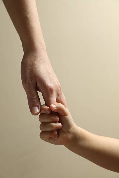 Mother and child holding hands on beige background, closeup
