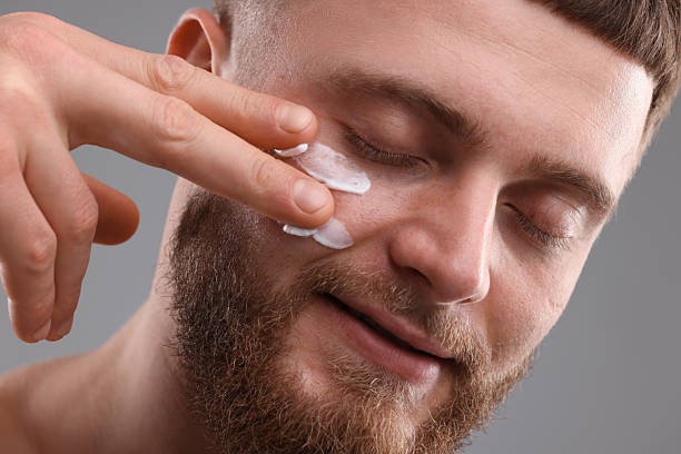 istock Handsome man applying moisturizing cream onto his face on grey background 2223482276