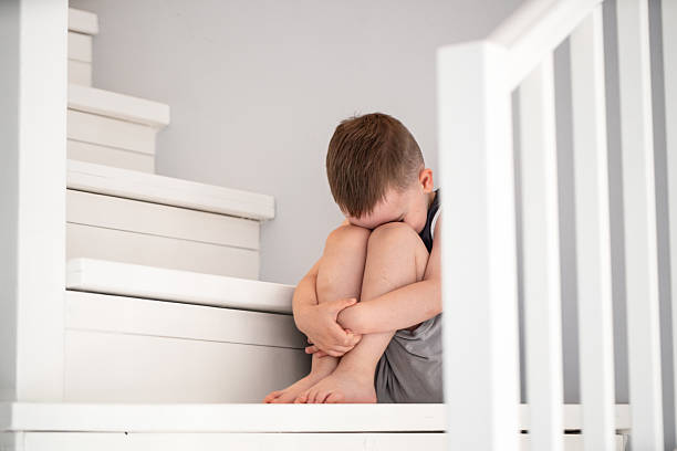 A young child sits in solitude on a white staircase, expressing feelings of sadness or distress