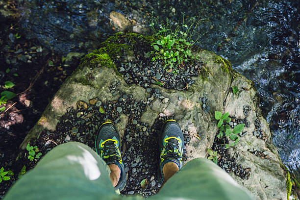 A vibrant scene showcasing a person's trekking sneakers on a wet rocky edge with a stream flowing below, emphasising adventure and nature.