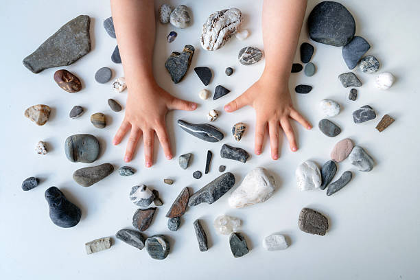 Children's hands and diverse colourful and textured stones on a white table surface, capturing a sense of creativity, exploration, and tactile interaction with natural materials.