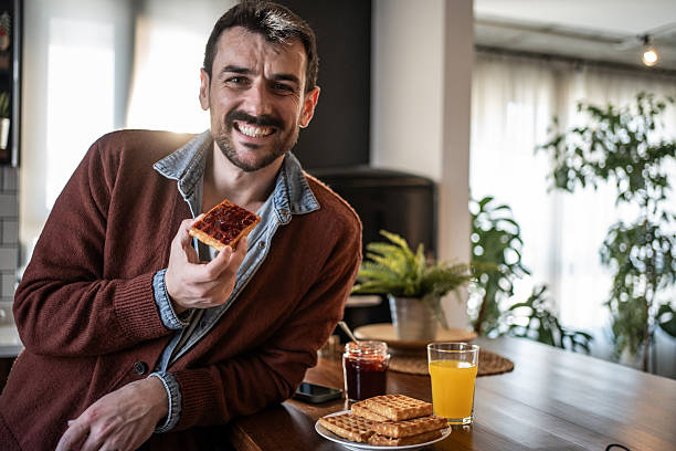 istock Smiling man enjoying waffles with jam for breakfast at home 2223486621