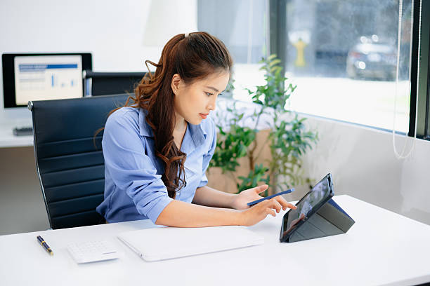 Young beautiful woman typing on tablet and laptop while sitting at the working white table