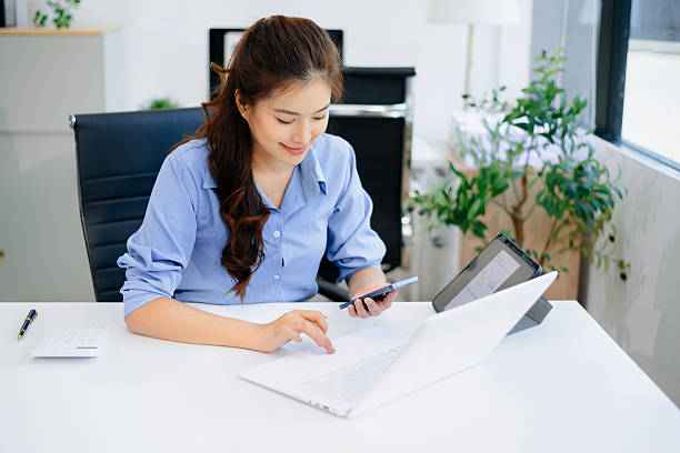 istock Young beautiful woman typing on tablet and laptop while sitting at the working white table 2223492415