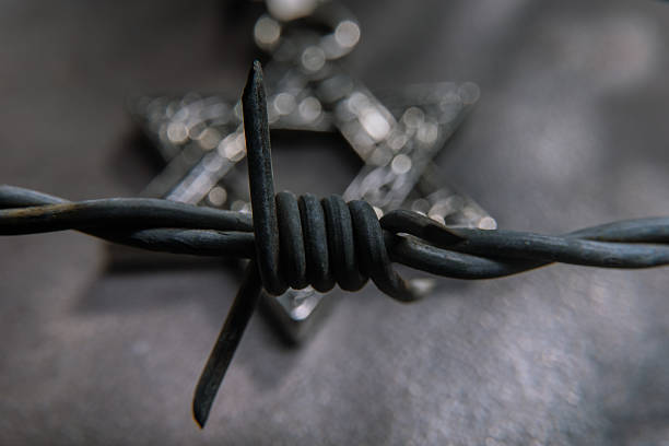 Close-up of a decorative Star of David pendant entangled behind barbed wire, symbolizing persecution, oppression, and resilience.