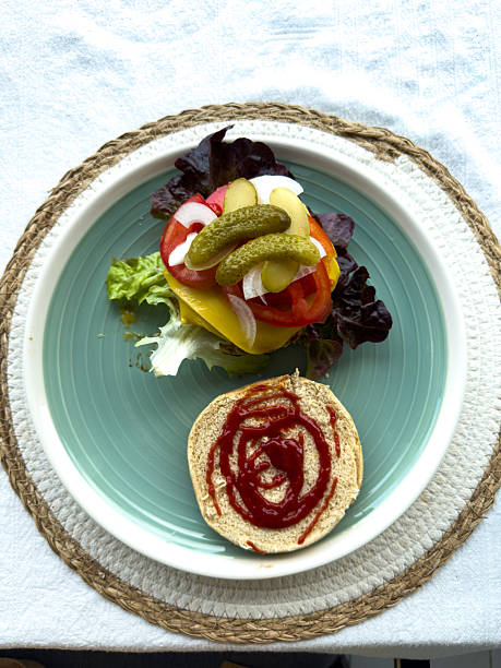 Open vegan sandwich with lettuce, tomato, pickles, onion, and vegan cheese on a bun. Fresh plant-based ingredients for healthy meals. Colorful vegetable sandwich on a plate.