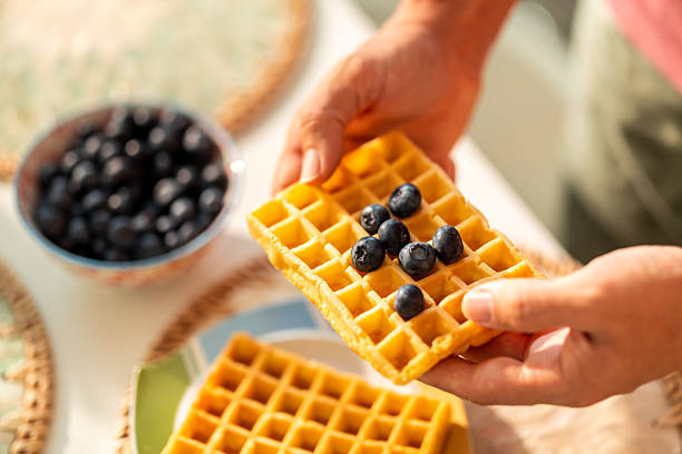 Close-up of hands holding a golden waffle with scattered fresh blueberries, ready to be served for breakfast or snack.