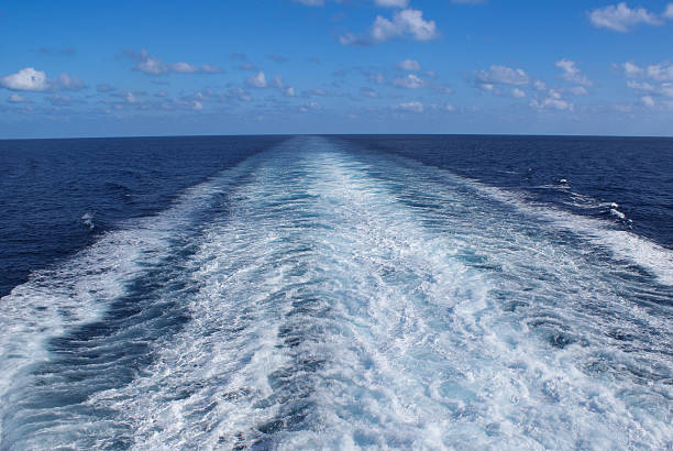 White wake trailing behind a ship sailing on a vast blue ocean under a cloudy sky, evoking a sense of journey and adventure