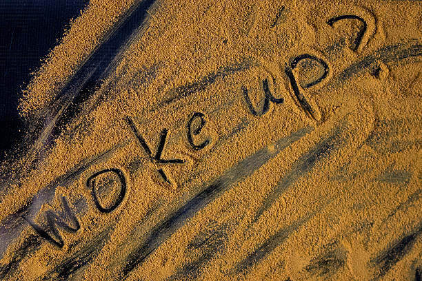 Close-up view of the conceptual phrase Woke up drawn with dark markings on a rough brown powder, representing a fresh start and conscious awareness