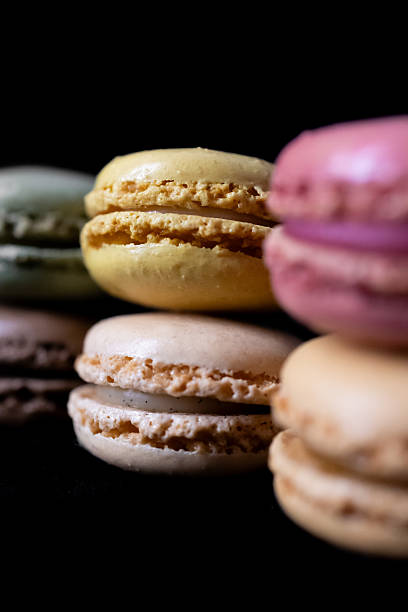 Colorful gourmet French macarons elegantly stacked against a deep dark background, representing delightful sweet treats and confectionery indulgence