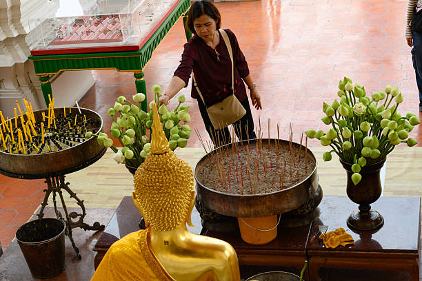Bangkok, Thailand. February 20th 2025.A Thai visitor lights a candle and makes an offering of a white lotus flower at The Wat Suthat Thepwararam Temple, Bangkok.