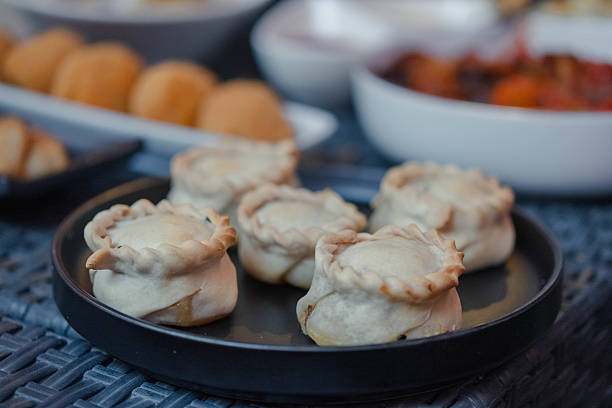 Aperitif served outdoors. In the foreground Panadinas, a traditional sardinian finger food, in the background a series of tapas and finger food. Concept of conviviality and being together