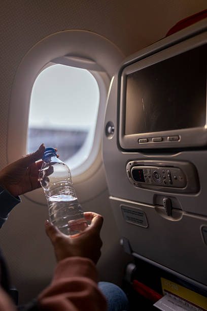 istock Unrecognizable female hand opens plastic water bottle near airplane window 2223513453