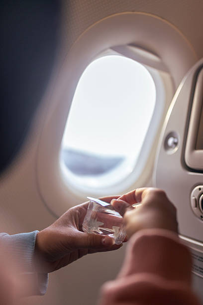 An unrecognizable female hand opens a drink during an airplane flight. The drink is in a disposable cup