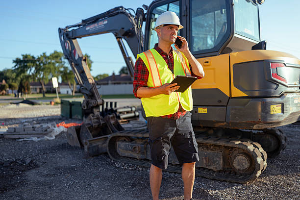 istock Worker with protective safety helmet and reflective vest using smartphone and digital tablet for project planning and checking schedule at construction site 2223513476
