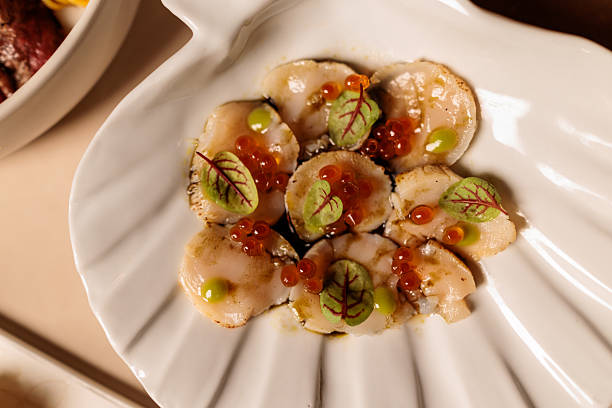 A close-up view of tender sea scallop carpaccio artfully presented on an elegant shell-shaped plate. In modern restaurant in Bangkok, Thailand.