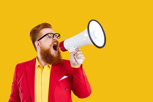 istock Bearded chubby man with loudspeaker in his hand makes loud advertisement on yellow background. 2223516387