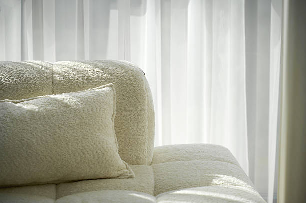 istock Cozy white couch with soft pillow beside sheer white curtains in bright sunlight 2223518092