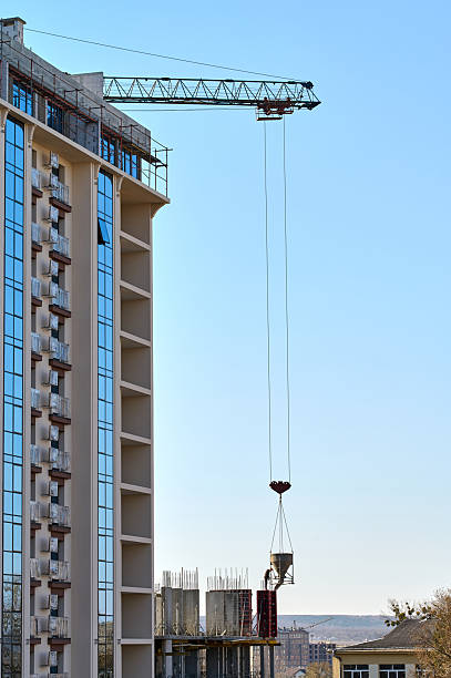Workers use a crane to lift construction materials at a high-rise building site during bright daylight.