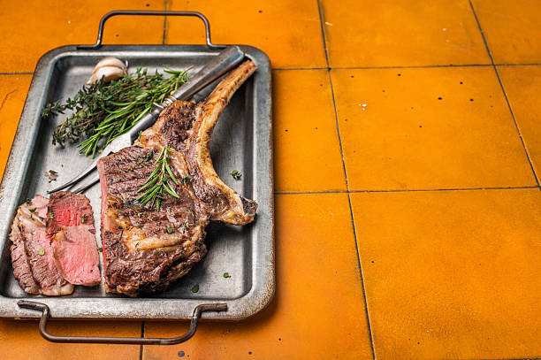 BBQ cooked Tomahawk beef steak, prime  ribeye with bone on tray with herbs. dark background. top view.