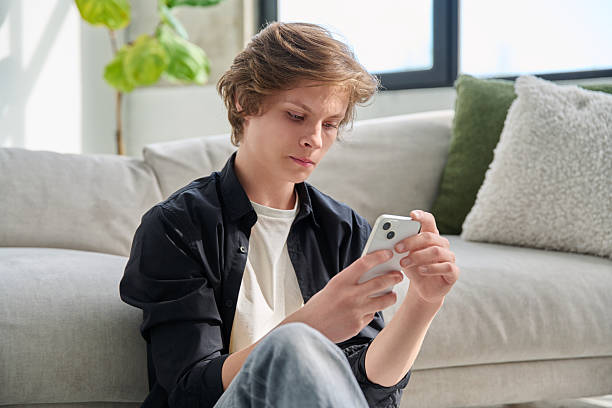 istock Serious handsome teenager guy using smartphone sitting on floor at home. 2223520041