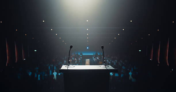 istock Modern Conference Stage With Two Microphones Under Spotlight, Ready for a Speaker to Come Up on Stage in a Dark Lit Auditorium. Public Speaking and Conference Presentation Concept 2223522726