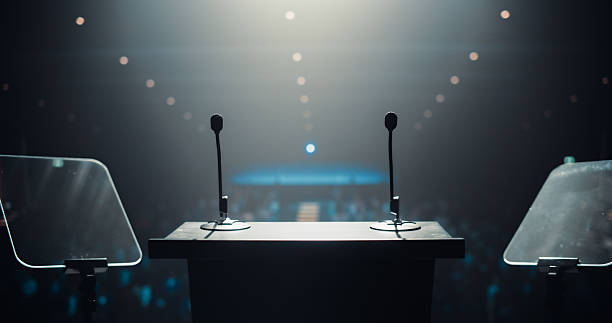 istock Sophisticated Conference Stage With Two Microphones Under Spotlights, Ready for a Speaker to Come Up on Stage in a Dimly Lit Auditorium. Public Speaking and Conference Presentation Concept 2223523667