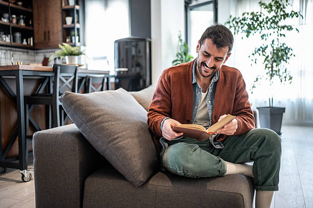istock Young man relaxing on sofa reading a book at home 2223527243