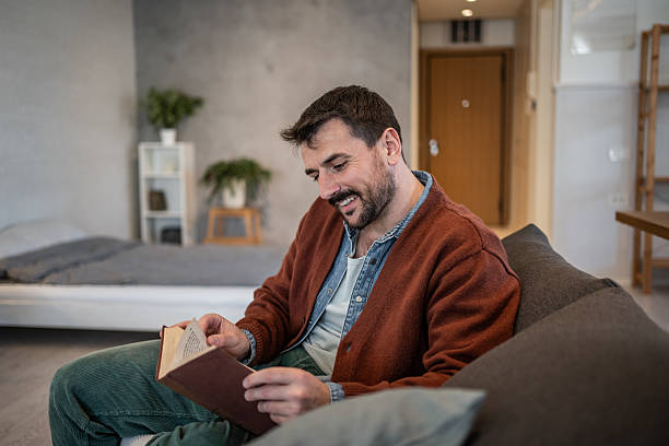 istock Smiling man reading a book at home on the sofa 2223527245