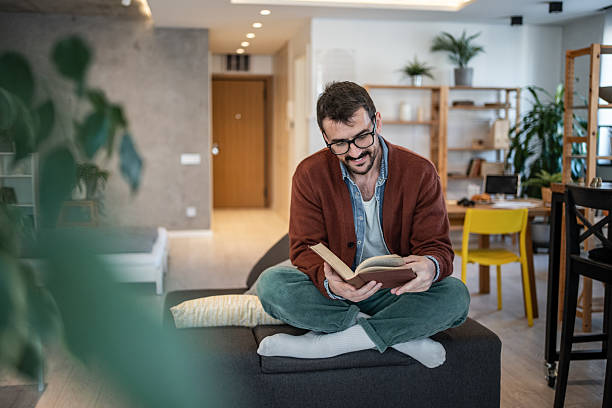 istock Young man reading a book at home on the couch 2223527272